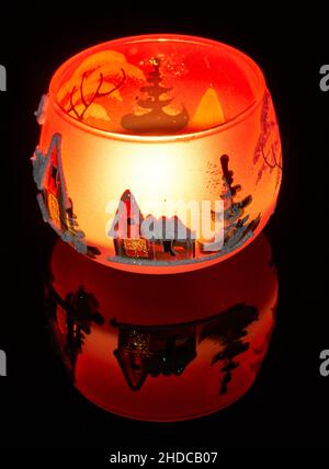 Eine handbemalte Glaskanne mit Winterlandschaft, die von einer Kerze im Inneren der Tasse angezündet wird. Eine Nahaufnahme und die Verwendung von Lichtmalerei. Stockfoto