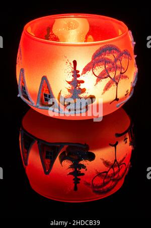 Eine handbemalte Glaskanne mit Winterlandschaft, die von einer Kerze im Inneren der Tasse angezündet wird. Eine Nahaufnahme und die Verwendung von Lichtmalerei. Stockfoto
