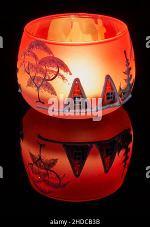Eine handbemalte Glaskanne mit Winterlandschaft, die von einer Kerze im Inneren der Tasse angezündet wird. Eine Nahaufnahme und die Verwendung von Lichtmalerei. Stockfoto