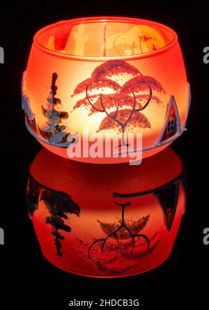 Eine handbemalte Glaskanne mit Winterlandschaft, die von einer Kerze im Inneren der Tasse angezündet wird. Eine Nahaufnahme und die Verwendung von Lichtmalerei. Stockfoto