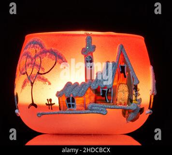 Eine handbemalte Glaskanne mit Winterlandschaft, die von einer Kerze im Inneren der Tasse angezündet wird. Eine Nahaufnahme und die Verwendung von Lichtmalerei. Stockfoto