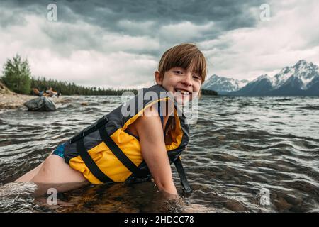 Glückliches junges Mädchen liegt in Bergsee mit Schwimmweste Stockfoto