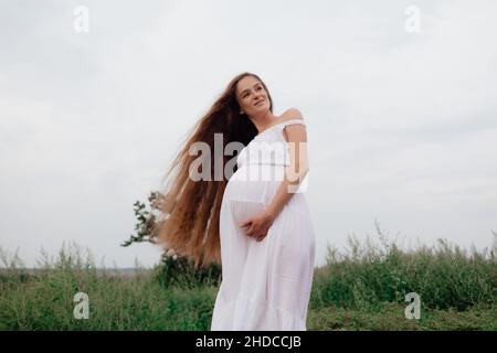 Glückliche Schwangere in weißem Kleid auf einer grünen Wiese Stockfoto