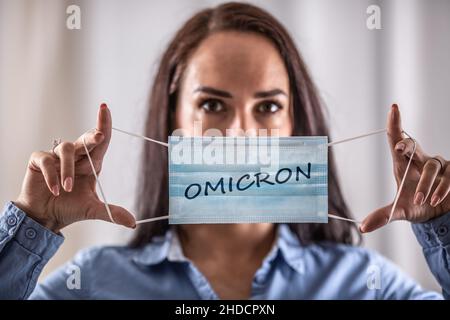 Eine junge Frau zieht eine Schutzmaske mit der Aufschrift Omicron an. Stockfoto