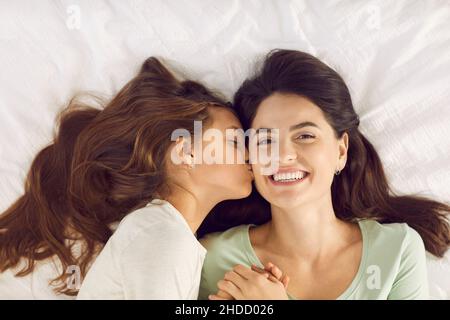 Die kleine Tochter weckt ihre glückliche Mutter am Morgen des Muttertages mit einem Kuss Stockfoto