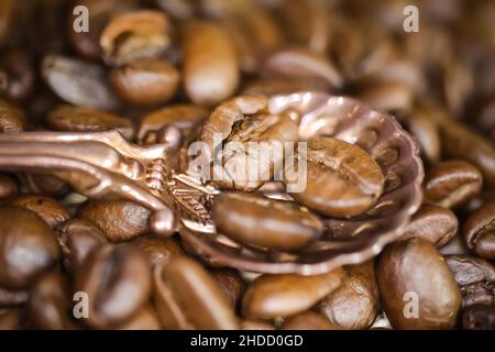 Makro-Nahaufnahme von vintage Bronze Löffel mit drei gerösteten Kaffeebohnen, verschwommener Hintergrund Stockfoto