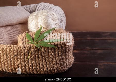 Fäden, Garn und Stoff aus Hanf mit Cannabisblatt auf Holzgrund. Stockfoto