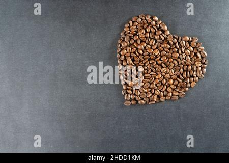 Herz aus gerösteten braunen Kaffeebohnen als Symbol der Liebe zum warmen Getränk auf einem schwarz-grauen strukturierten Hintergrund Stockfoto