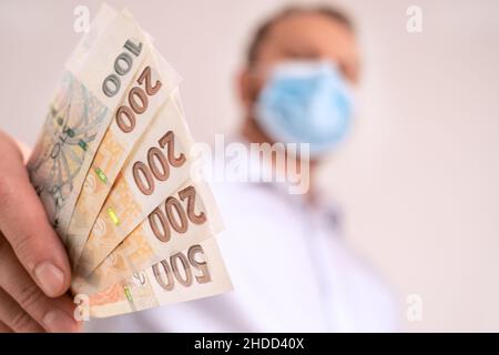 Fan von Cash Tschechische republik Krone. Finanzierung während des Coronavirus in Tschechien Konzept. CZK kleine Banknoten. Mann in einer schützenden medizinischen Gesichtsmaske hält kro fest Stockfoto