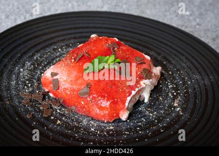 Herzhafte Erdbeer-Tiramisu auf einem schwarzen Teller mit Pfefferminze, Puderzucker und Schokoladenstreuseln Stockfoto