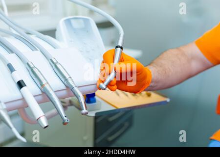 Männliche Zahnarzthand in orangefarbenen Handschuhen, die mit der Zahnbohrmaschine arbeiten Stockfoto