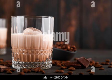 Glas irischer Rahm-Baileys-Likör mit gerösteten Kaffeebohnen, Zimt und Schokolade auf dunklem Holz-Hintergrundtisch. Selektiver Fokus. Stockfoto