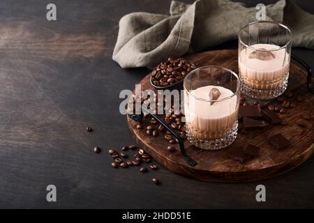 Glas irischer Rahm-Baileys-Likör mit gerösteten Kaffeebohnen, Zimt und Schokolade auf dunklem Holz-Hintergrundtisch. Selektiver Fokus. Stockfoto