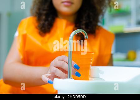 Teenager-Mädchen hodling Kunststoff orange Farbe Tasse Wasser in der Zahnarztpraxis, um den Mund spülen Stockfoto