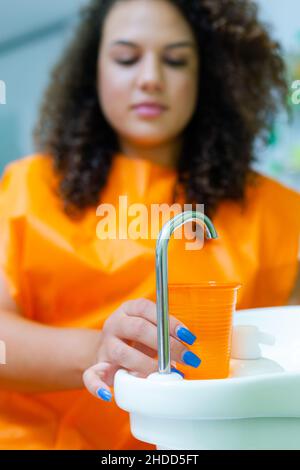 Teenager-Mädchen hodling Kunststoff orange Farbe Tasse Wasser in der Zahnarztpraxis, um den Mund spülen Stockfoto