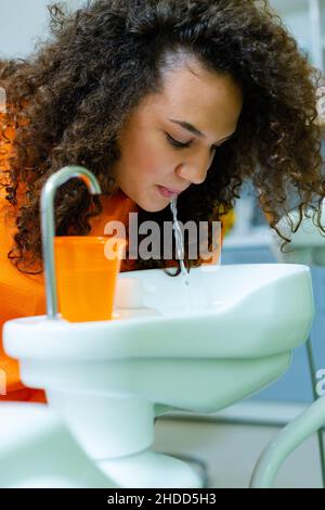 Teenager-Mädchen spülen Mund nach der Behandlung in der Zahnarztpraxis, spucken Wasser in cuspivor - Keramik-Schüssel Stockfoto