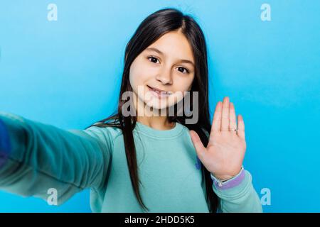 Portrait von glücklichen freundlichen kleinen Mädchen auf blauem Hintergrund unter Selfie Welle hallo Stockfoto