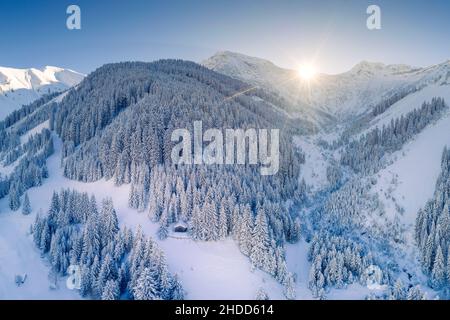 Einsame Einzelhütte auf Waldlichtung in verschneiten österreichischen Bergen im Winter mit Sonnenstrahlen auf Bergrücken Stockfoto