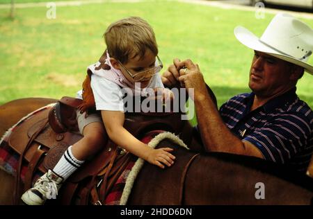 Austin Texas USA, 1992: Männlicher Helfer hilft behinderten Kindern beim Reiten eines Pferdes im Rahmen eines Therapieprogramms für behinderte Kinder. ©Bob Daemmrich Stockfoto