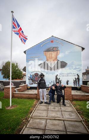 Jugendliche posieren vor politischen Wandgemälden mit paramilitärischen Symbolen auf dem Lower Shankill Estate, Belfast. Stockfoto