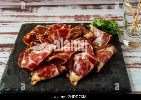 Zerkleinerte Ansicht eines exquisiten Fetas de Bondiola oder rohes eingelegtes Schweinefleisch auf einer schwarzen Platte. Stockfoto