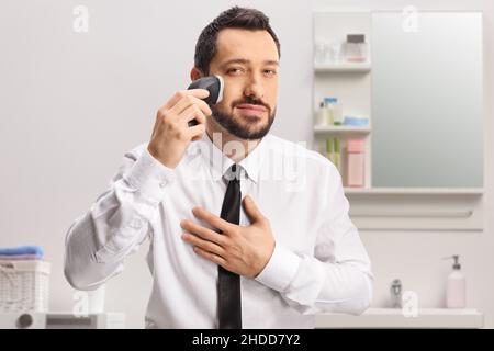 Mann in einem Hemd und Krawatte mit einer Rasiermaschine im Badezimmer Stockfoto