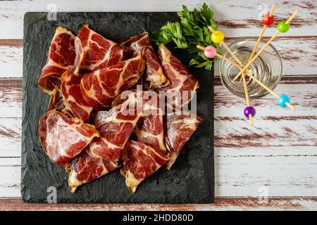 Blick von oben auf einige exquisite Fetas de Bondiola oder rohes eingelegtes Schweinefleisch auf einer schwarzen Platte auf einem rustikalen Tisch. Stockfoto
