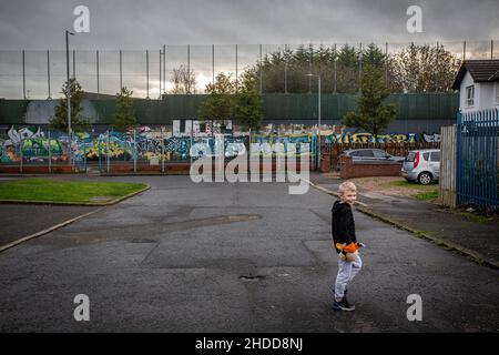 Kleiner Junge mit farbenfrohen Wandgemälden und Graffiti auf Peace Wall oder Peace Line, der auf dem Cupar Way in Belfast entlang läuft, die überwiegend republikanische und trennen Stockfoto