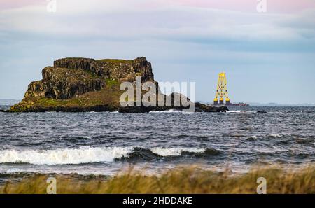 Firth of Forth, Schottland, 5th. Januar 2022. Wetter in Großbritannien: Bei Sonnenuntergang fährt ein Lastkahn mit einer riesigen Windturbinenplattform zur Nordsee, vorbei an Fidra Island Stockfoto