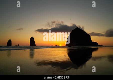 Sonnenuntergang am Haystack Rock Cannon Beach. Sonnenuntergang am Haystack Rock in Cannon Beach, Oregon, während die Brandung am Strand aufgeht. Usa. Stockfoto