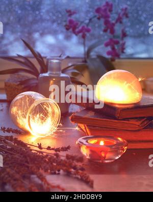 Magische Lichter mit Funkeln, orange leuchten in verschiedenen Gläsern. Winterzeit mit Lichtern und alten Büchern. Stapel alter alter Bücher. Exotische Pflanzen, Orchidee Stockfoto