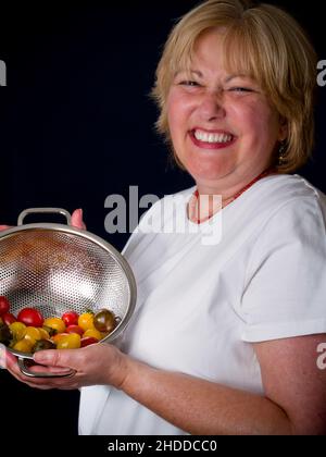 Lächelnde reife Frau mit Kirschtomaten in einem Ablagefisch Stockfoto