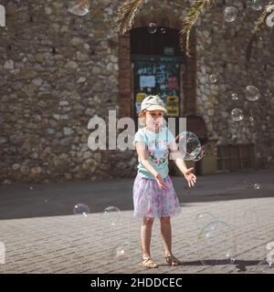 Hübsches kleines Mädchen spielt mit großen Blasen in der Straße am Sommertag, Spanien Stockfoto