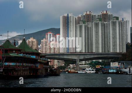 Jumbo Kingdom, ein schwimmendes Restaurant, mit der Kulisse des Aberdeen Floating Village und den Turmblöcken dahinter, Hongkong. Stockfoto
