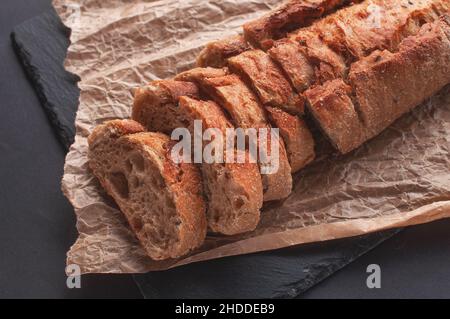 Baguette aus Buchweizenmehl ohne Hefe auf schwarzem Hintergrund, geschnittenes Brot auf Pergamentpapier. Stockfoto