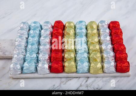 Runde Schokoladenkugeln mit Aluminiumfolie in Box-Behälter auf Marmorboden. Minimalistische, festliche Frühlingskomposition. Weicher selektiver Fokus, Stockfoto