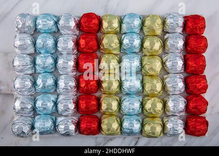 Runde Schokoladenkugeln mit Aluminiumfolie in Box-Behälter auf Marmorboden. Minimalistische, festliche Frühlingskomposition. Weicher selektiver Fokus, Stockfoto