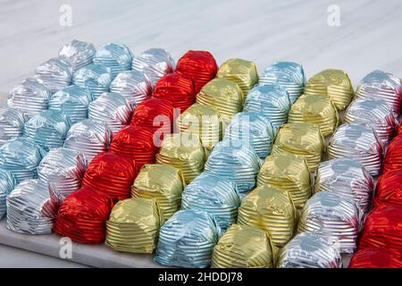 Runde Schokoladenkugeln mit Aluminiumfolie in Box-Behälter auf Marmorboden. Minimalistische, festliche Frühlingskomposition. Weicher selektiver Fokus, Stockfoto