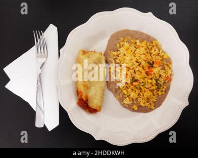 Traditionelles mexikanisches Essen, Tamale-Reis und gebratene Bohnen auf weißem Teller mit schwarzem Hintergrund. Stockfoto