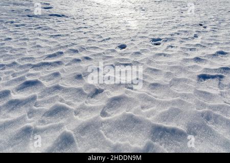 Der vom Wind gewellte Schnee schafft kleine Reliefs auf der Erdoberfläche in den Bergen. Hintergrund mit Textur. Stockfoto