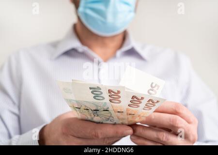 Zählen kleine Geldscheine der Tschechischen Republik Koruna. Finanzierung während des Coronavirus in Tschechien Konzept. CZK kleine Banknoten. Mann in einer schützenden Medica Stockfoto
