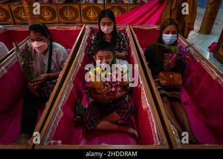 Bangkok, Thailand. 31st Dez 2021. Die thailändische Familie wird als Teil des Auferstehungsrituals im Tempel in Särgen sitzend gesehen.Devotees werden in einem jährlichen Neujahrsritual im Wat Takien in der Nähe von Nonthaburi wiederbelebt. Dieser Ritus beginnt mit einem Gebet, gefolgt von den Teilnehmern, die mit heiligen Fäden um ihren Kopf gewickelt singen, bevor sie sich in einen Sarg legen, um zu „sterben“ und gereinigt zu werden. Kredit: SOPA Images Limited/Alamy Live Nachrichten Stockfoto