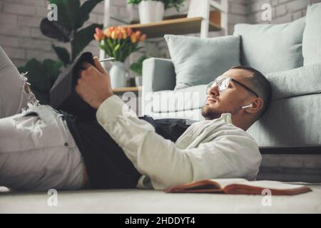 Mann, der auf dem Boden lag und sein Tablet hielt, während er von zu Hause aus arbeitete. Kommunikationstechnologie. Internet-Technologie. Stockfoto