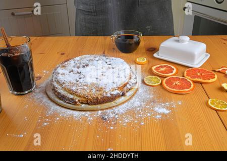 Man streut Puderzucker auf hausgemachten Kuchen. Ein Holztisch und Küche Hintergrund Stockfoto