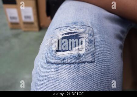 Nahaufnahme einer Jeans mit Loch am Knie. Eine Lösung von zerrissenen Jeans mit einem Fleck von ähnlichen Farben Tuch hinter. Stockfoto