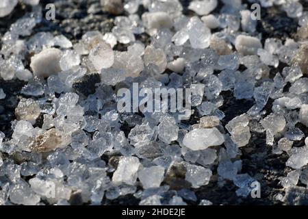 Makroansicht von Eis und Schnee schmelzen Salzkristalle auf einem Asphaltweg im Winter. Stockfoto