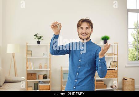 Glücklicher männlicher Hausbesitzer, der sich mit dem erfolgreichen Immobilienkauf rühmt und Schlüssel zu seinem neuen Zuhause zeigt. Stockfoto