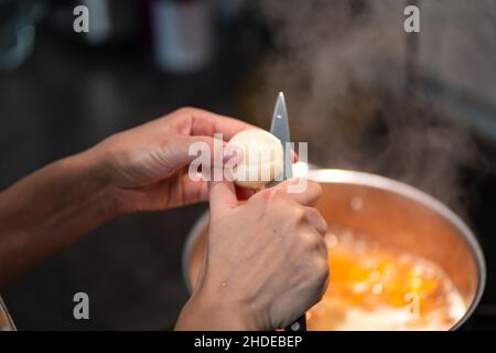 Die Hände der Frau schneiden eine Zwiebel mit einem Messer in zwei Hälften. Stockfoto