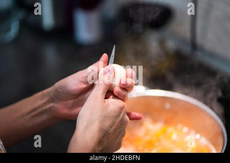 Die Hände der Frau schneiden eine Zwiebel mit einem Messer in zwei Hälften. Stockfoto