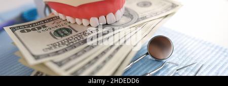 Zahnärztliches künstliches Kieferinstrument und hundert Dollar-Scheine auf dem Zahnarzttisch Stockfoto